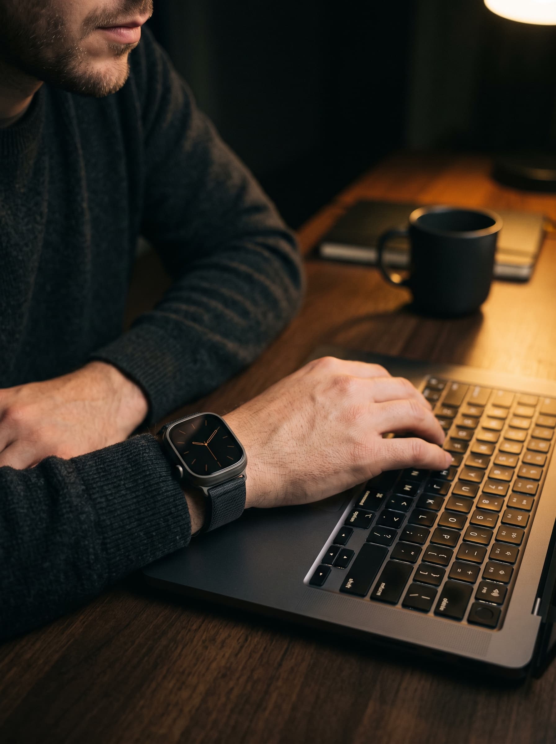 Epoch One on a wrist beside a laptop keyboard under warm lamp light